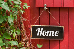 A black sign hanging at a red wall saying Home